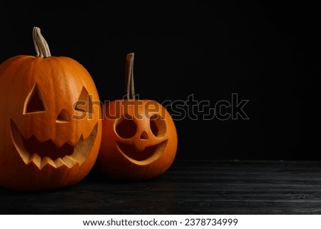 Scary jack o'lanterns made of pumpkins on wooden table against black background, space for text. Halloween traditional decor