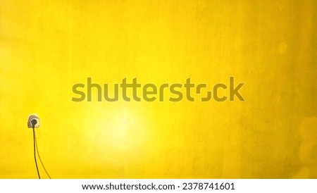 The background is a yellow-orange wall with a socket and cable
