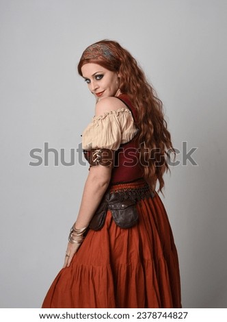 close up portrait of beautiful red haired woman wearing a medieval maiden, fortune teller costume. Posing with gestural hands reaching out, dancing, isolated on studio background.
