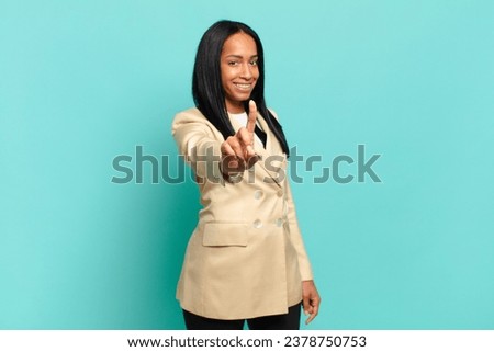 young black woman smiling proudly and confidently making number one pose triumphantly, feeling like a leader. business concept