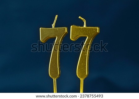 close up on the gold number seventy-seventh candle on a dark background.