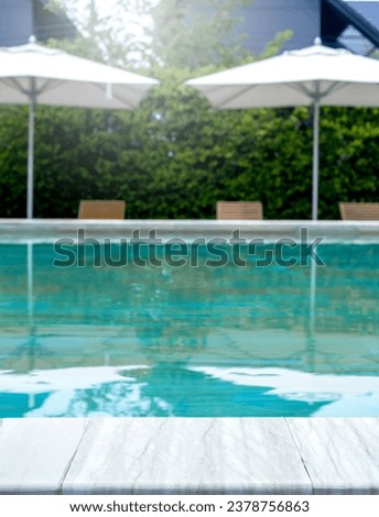 Summer pool background. Empty space on the pool edge, marble stone tiles and blurred swimming pool with beach umbrellas in tropical resort, summer background, vertical style.