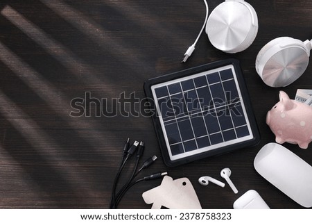 Solar panel, electronic devices and piggy bank on wooden background, space for text