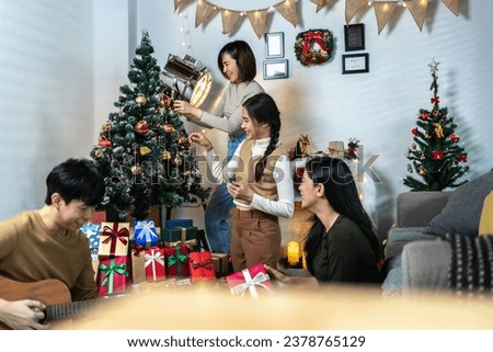 A group of Asian friends share laughter and joy as they decorate a Christmas tree. Amidst the festive setting, wrapped gifts, and twinkling lights, they create memories to cherish