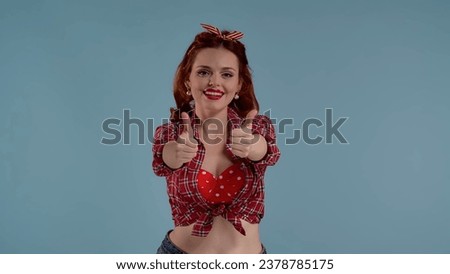 In the frame on a blue background is a young red-haired girl with bright makeup. She is looking at the camera and smiling, leaning forward slightly. Demonstrates with both hands a gesture of cool HDR
