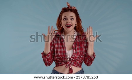 In the shot, a young red-haired woman with brightly colored makeup is seen against a blue background. She is looking at the camera to portray surprise, delight, excitement. HDR BT2020 HLG Material.