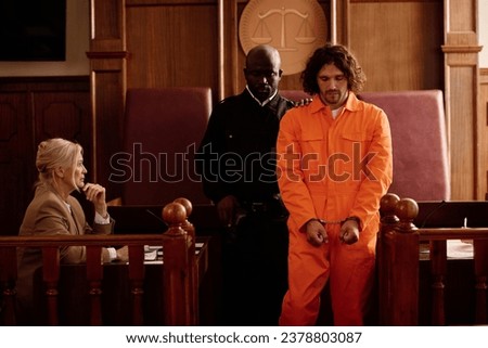 Young policeman standing next to male prisoner in cuffs and orange jumpsuit Royalty-Free Stock Photo #2378803087
