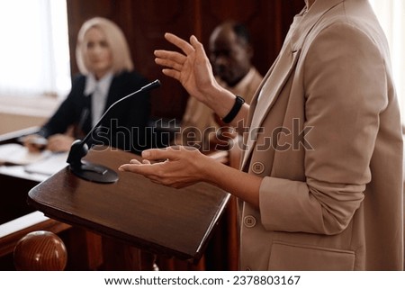 Cropped shot of young female witness in beige blazer standing by tribune Royalty-Free Stock Photo #2378803167