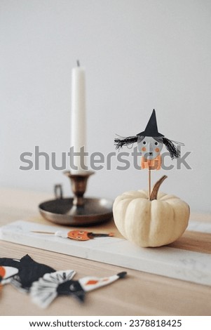 Halloween table composition with small white pumpkin with a witch head and a  gold candlestick in the background 