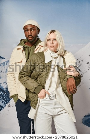 attractive stylish couple in seasonal outfits posing together with mountain backdrop, winter concept Royalty-Free Stock Photo #2378825021
