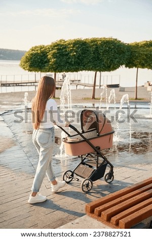 Young woman is with pram, walking outdoors.