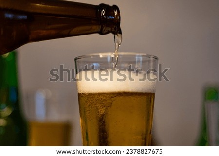 Close-Up. Pouring Beer In Glass. Beer is poured from dark brown bottle into beer glass.