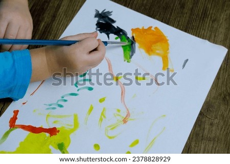 children's hand paints with brush, small child, little girl preschooler 3 years creates bright picture on paper, childish naive drawing in colored watercolor, gouache, acrylic, happiness childhood Royalty-Free Stock Photo #2378828929