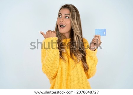 Beautiful hispanic blonde businesswoman wearing yellow sweater hold credit card point empty space
