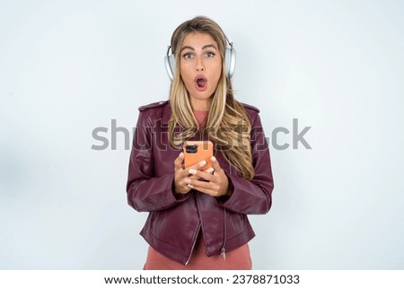 Portrait of an excited Beautiful hispanic blonde businesswoman wearing leather jacket playing games on mobile phone.