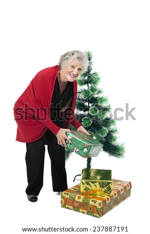 Old woman holding a christmas present while standing next to a tree 