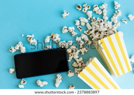 Yellow and white striped boxes with popcorn and phone on a blue background. Entertainment concept. Movie night with popcorn. Cinema theme.