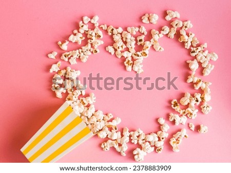 Yellow stripped popcorn box and popcorn in heart shape  on a pink background. TV watching concept with copy space. Movie night. Entertainment concept.