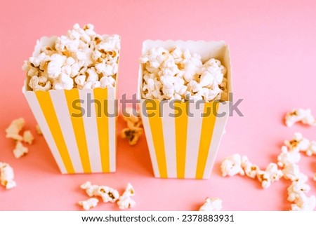 Yellow stripped popcorn box on a pink background. TV watching concept with copy space. Movie night. Entertainment concept.