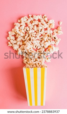 Yellow stripped popcorn box on a pink background. TV watching concept with copy space. Movie night. Entertainment concept.