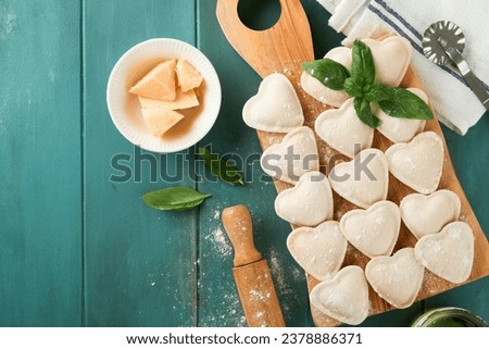 Italian ravioli pasta in heart shape.Tasty raw ravioli with flour and basil on old wooden blue background. Food cooking ingredients background. Valentines, Mothers Day lunch ideas. Top view copy space