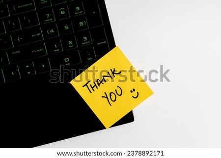 Top view of words thank you written on sticky note on keyboard over wooden background.
