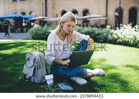 Caucasian female student using 4g internet for browsing web page in social networks during e learning in campus park, millennial hipster girl downloading multimedia on modern netbook computer