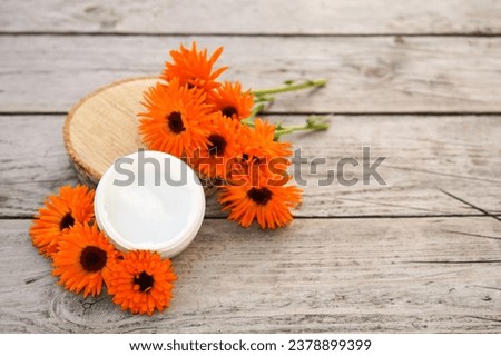 Fresh orange calendula flowers on a wooden background in nature. Cosmetic cream for cleansing the skin with calendula flowers. Medical Dermatology. Cream for body care with calendula.