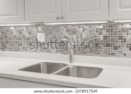 odern White Kitchen Interior with Steel Mosaic Backsplash, Under-Cabinet Lighting, and Sleek Stainless Steel Faucet