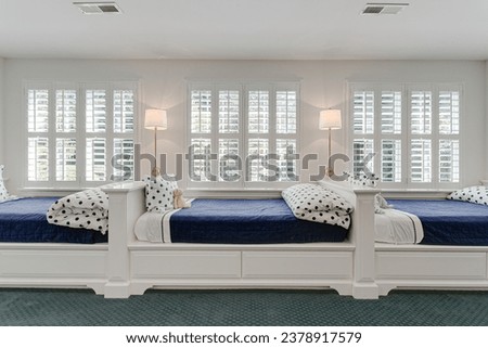 Bright Children's Bedroom with Twin Blue Bedding, Polka Dot Pillows, Classic White Plantation Shutters, and Elegant Stand Lamps Royalty-Free Stock Photo #2378917579