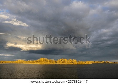 Dramatic and picturesque scene. Bright autumn landscape with thunderclouds over a pond. Artistic picture. The world of beauty and harmony.