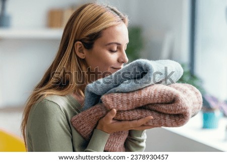 Shot of beautiful young woman holding and smelling clean clothes at home. Royalty-Free Stock Photo #2378930457