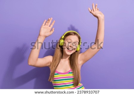 Photo portrait of cute teen blonde woman raise hands listen music dance wear trendy striped clothes isolated on purple color background