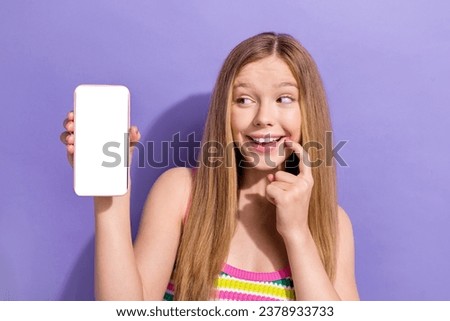 Photo portrait of pretty teenager blonde girl hold white screen device wear trendy striped outfit isolated on purple color background