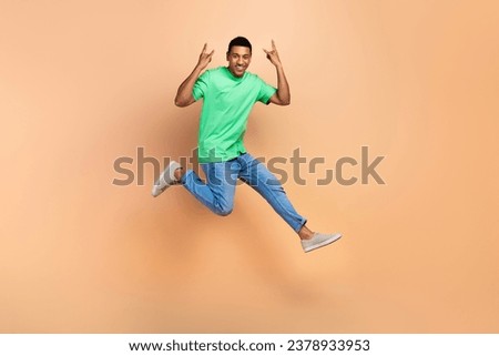 Full length photo of satisfied handsome man wear stylish t-shirt jeans jumping show horns symbol isolated on beige color background