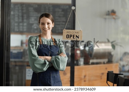 Happy young female owner standing with open sign at coffee shop, Smiling small business owner showing open sign. 