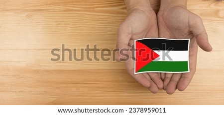 Palestine flag holding hand adult on wood background.
Concept conflict Israel vs Palestinian.
top view. 