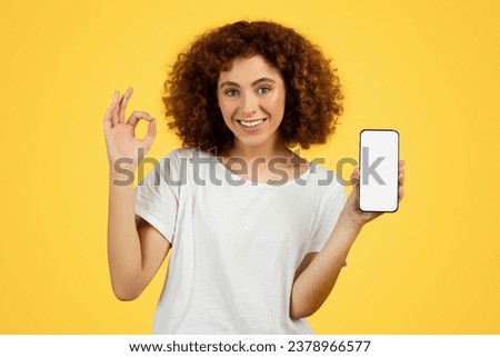 Glad young woman show phone with empty screen and ok sign hand, isolated on yellow background, studio. Good news, recommendation online sale and mobile app, approve ad and offer Royalty-Free Stock Photo #2378966577