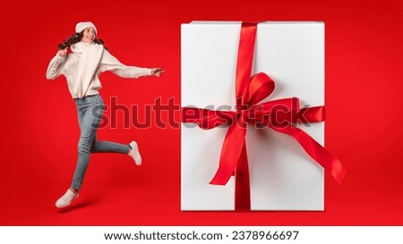 Energetic woman in winter clothes joyfully jumping beside a giant gift with ribbon bow on red background in studio. Festive excitement and holiday surprises offers. Collage, panorama