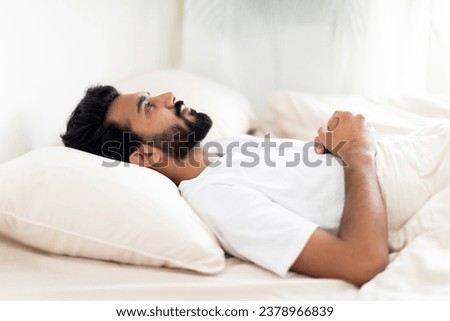 Insomnia Concept. Depressed indian man unable to sleep, lying in bed alone and looking at ceiling, young eastern guy suffering sleeplessness, mental health problem or male depression, copy space Royalty-Free Stock Photo #2378966839