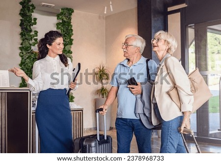 A senior couple is arriving at the hotel with luggage, and a smiling hotel representative is welcoming them Royalty-Free Stock Photo #2378968733