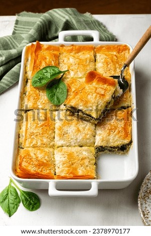 Casserole with Spanakopita, homemade Greek savory spinach pie, which contains cheese feta, chopped spinach, green, egg, layered in phyllo or filo pastry. Vertical image. Royalty-Free Stock Photo #2378970177