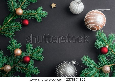 Christmas frame made of fir branches with Christmas balls on black background. Top view, flat lay, copy space.
