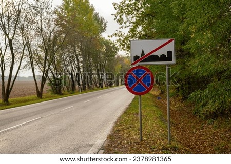 Road signs by the road: parking ban and a board marking the end of the built-up zone, trees by the road, autumn