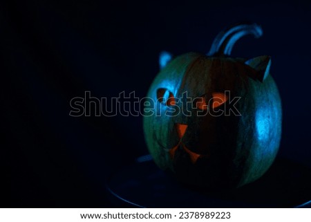Halloween pumpkin with cat-like face and orange candle glow in blue light