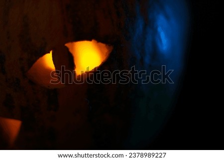 Closeup of Halloween pumpkin with cat-like eye glowing in orange candle light inside