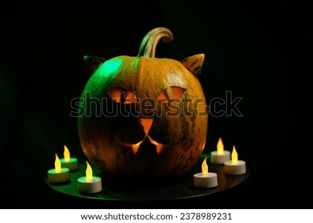 Halloween pumpkin with cat-like face and orange candle glow in green light