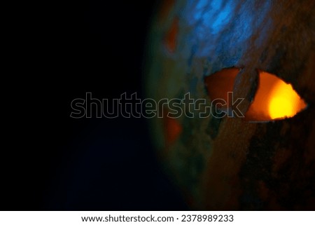 Closeup of Halloween pumpkin with cat-like eye glowing in orange candle light inside