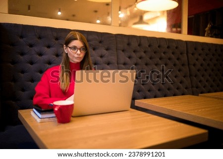 Serious woman successful blog editor having online work on notebook gadget while sitting in coffee shop interior near copy space for advertising 