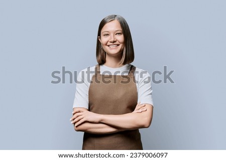 Portrait of young smiling confident woman in apron on grey background